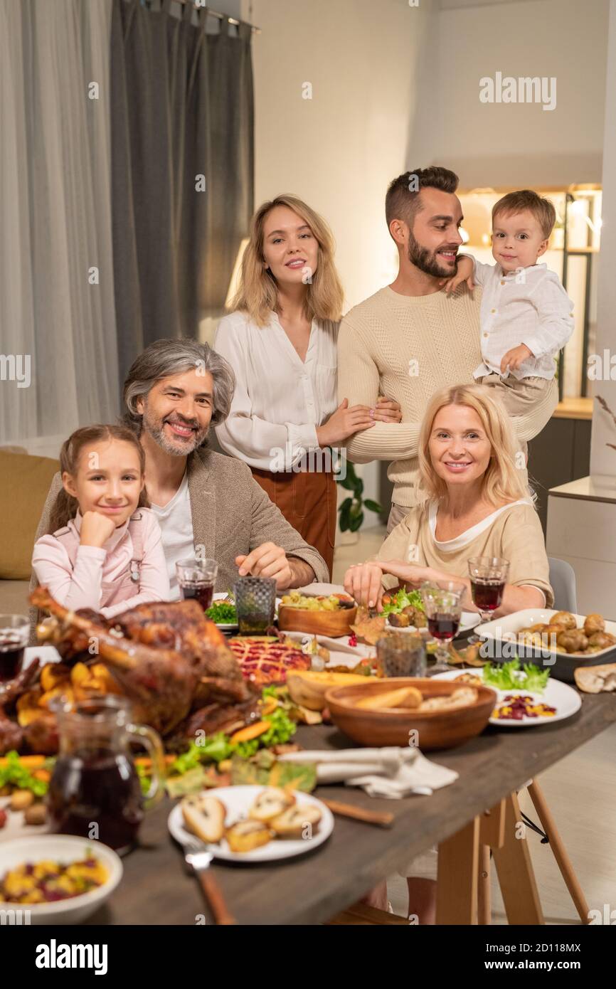 Large family of three generations sitting by table served by variety of food Stock Photo