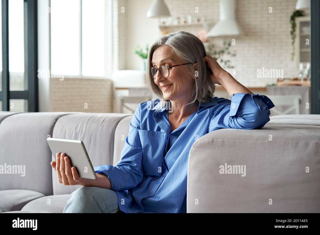Happy 60s mature woman calling or watching video digital tablet at home. Stock Photo