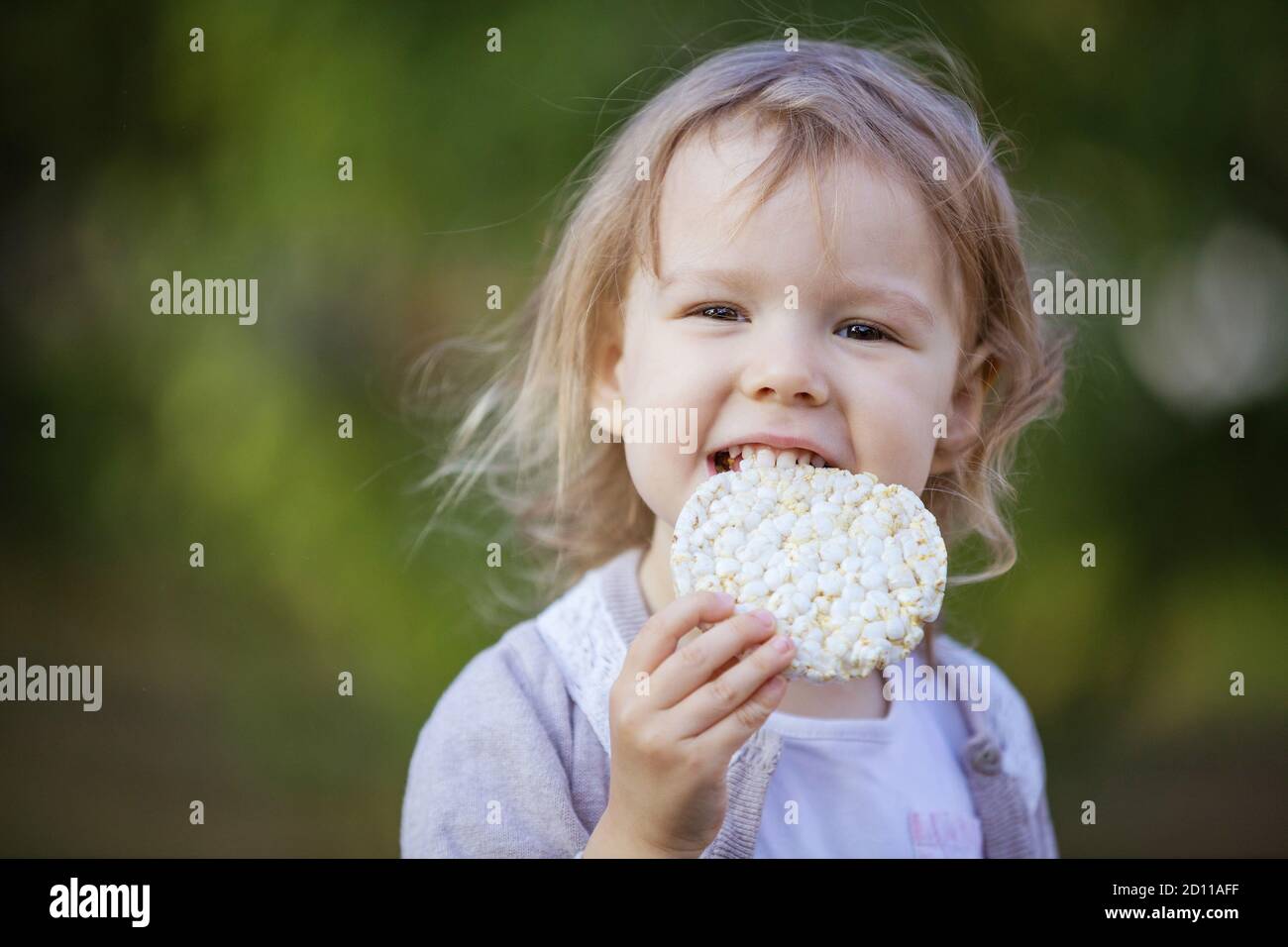 Happy little girl eating corn cracker in summer park Stock Photo Alamy