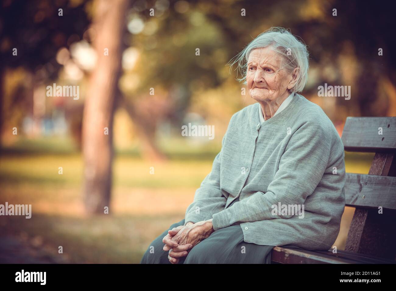 Portrait of senior woman sitting on bench in autumn park. Old lady feeling lonely and sad. Frustrated aged female outdoors. Stock Photo