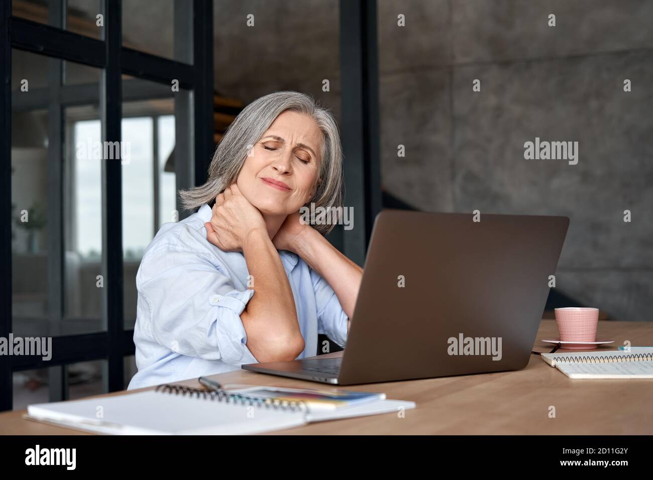 Tired stressed older mature business woman suffering from neck pain. Stock Photo