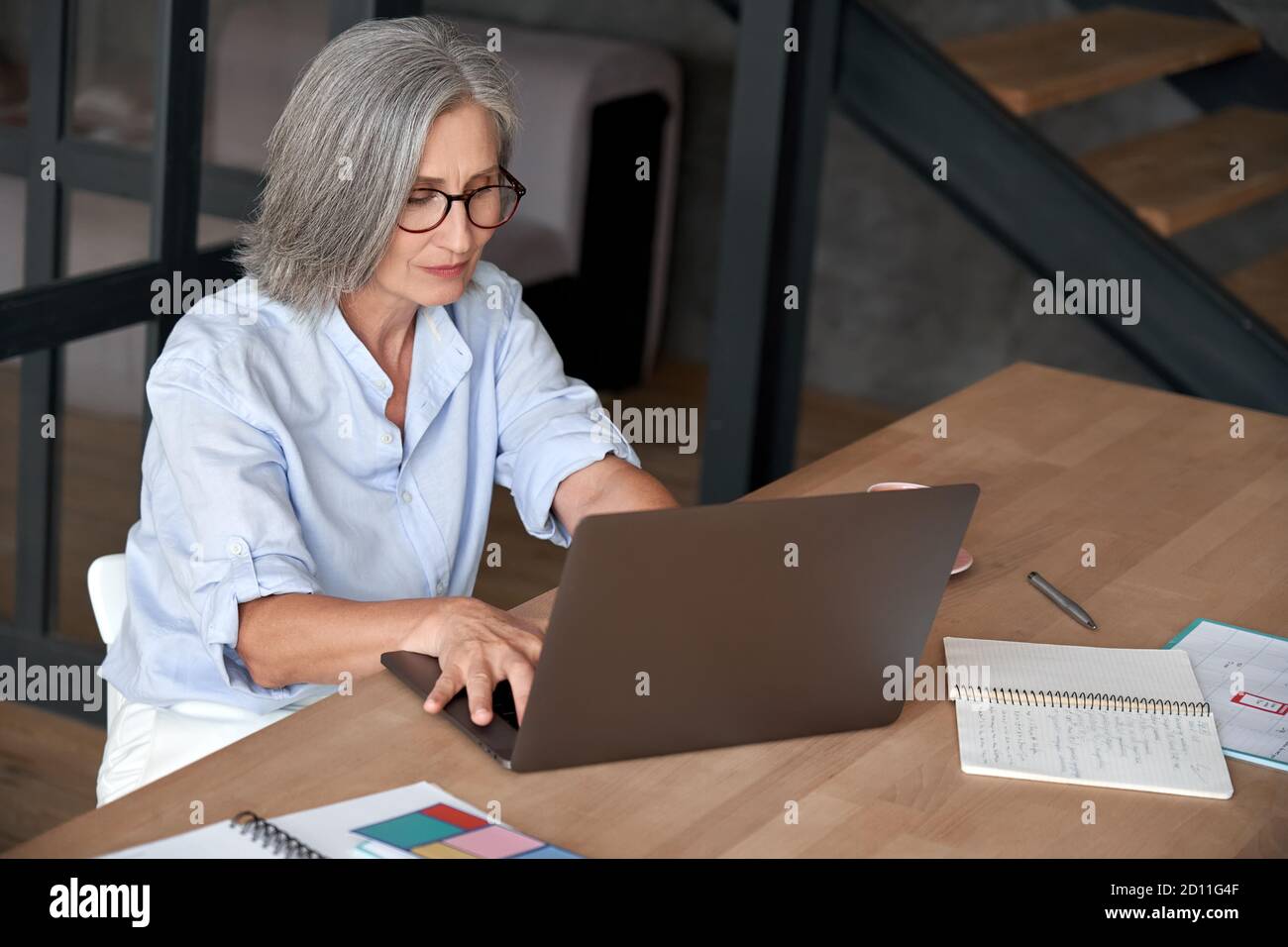 Older mature middle aged woman using laptop computer sitting at work desk. Stock Photo