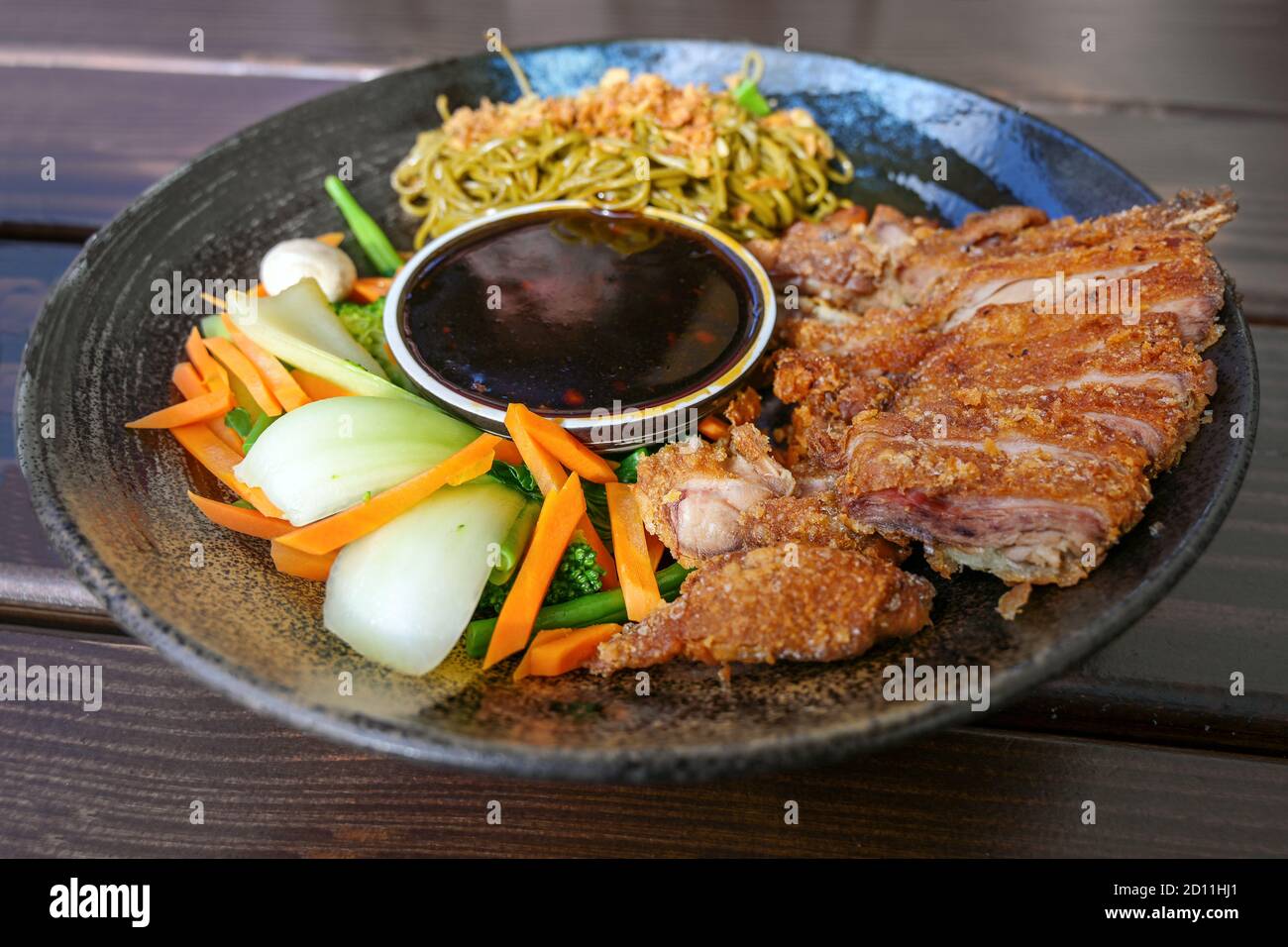 Asian dish with roasted duck, vegetables, noodles and teriyaki sauce in a flat bowl on a wooden table, selected focus, narrow depth of field Stock Photo