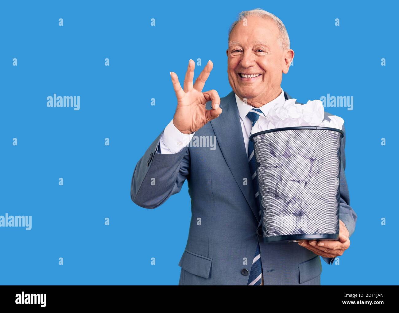 Senior handsome grey-haired man holding paper bin with crumpled document doing ok sign with fingers, smiling friendly gesturing excellent symbol Stock Photo