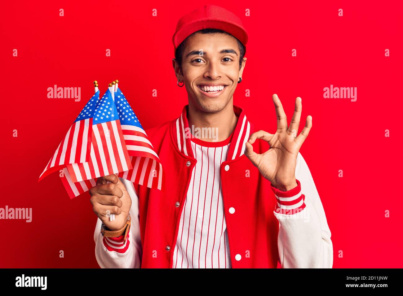 Young african amercian man wearing baseball uniform holding america flags doing ok sign with fingers, smiling friendly gesturing excellent symbol Stock Photo