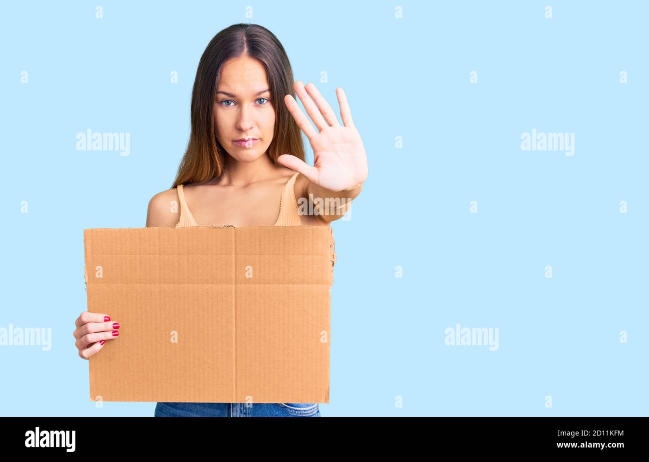 Beautiful brunette young woman holding cardboard banner with blank space with open hand doing stop sign with serious and confident expression, defense Stock Photo