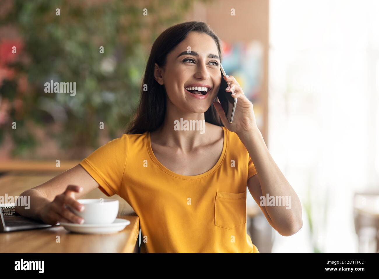 Happy lady talking on phone while drinking coffee at cafe Stock Photo