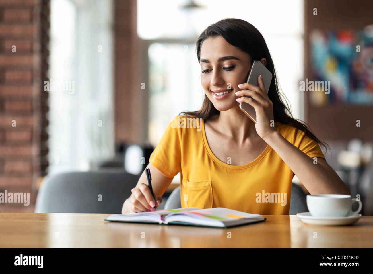 Young lady talking on smartphone while drinking tea at cafe Stock Photo