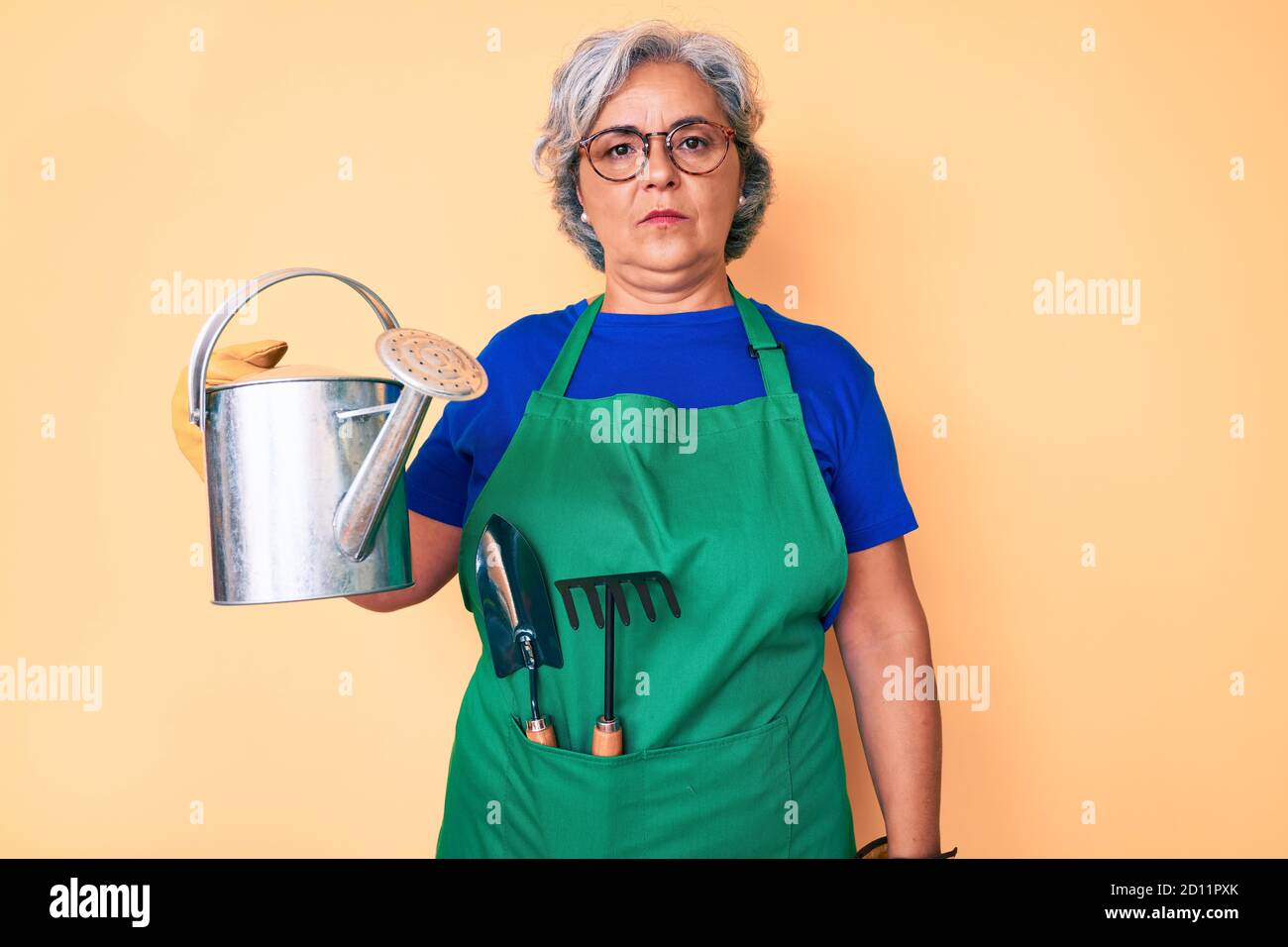 Senior hispanic grey- haired woman wearing gardener apron and gloves ...