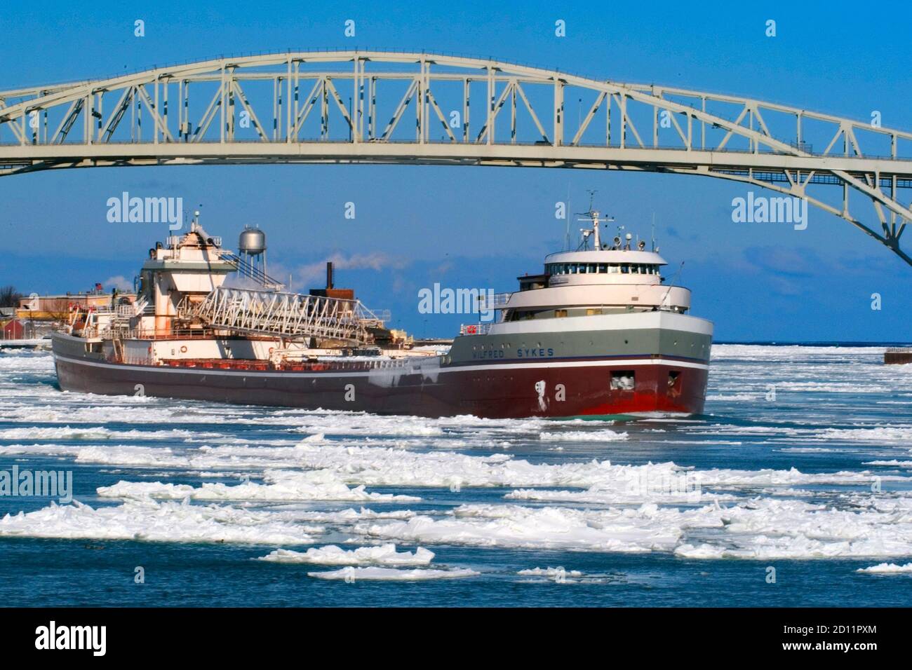 The Wilfred Sykes lake Freighter negotiating ice  on the St. Clair River under the Blue Water International Bridge at Lake Huron, Michigan Stock Photo