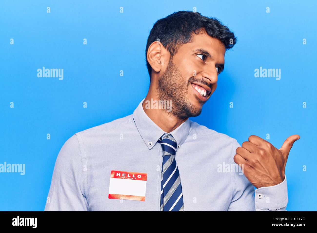 Young latin man wearing sticker with hello my name is message pointing ...
