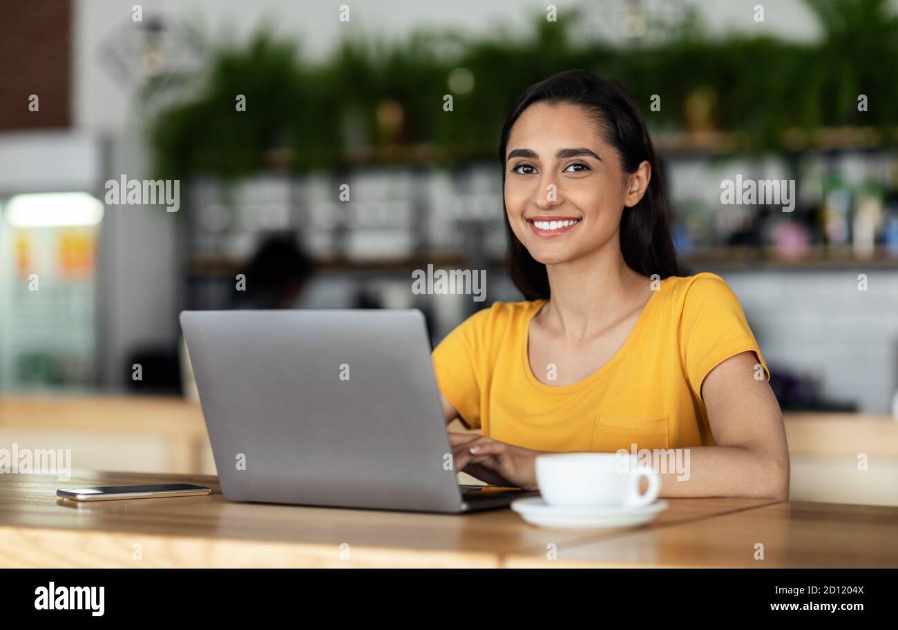 Cheerful female student using laptop at cafe Stock Photo