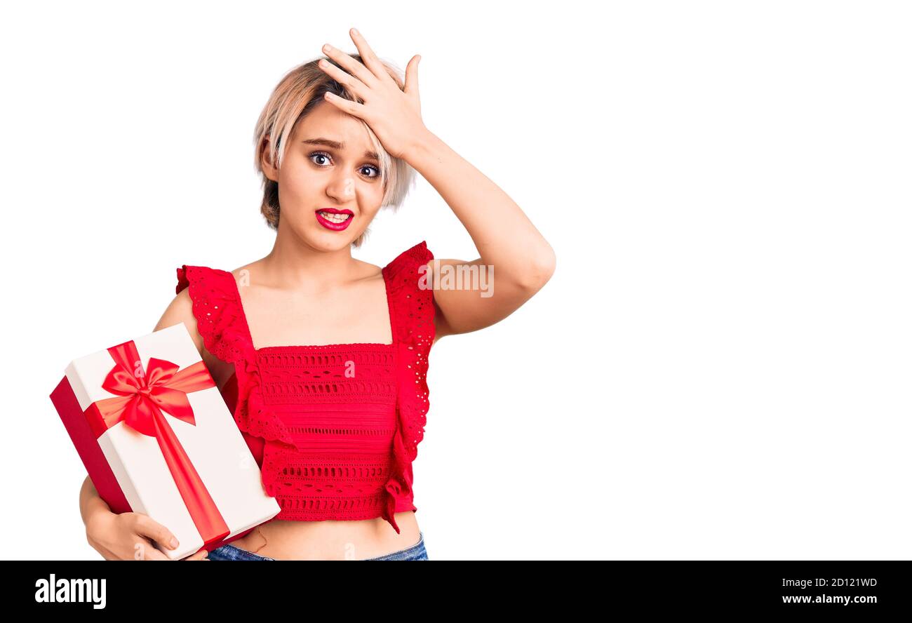 Young beautiful blonde woman holding gift stressed and frustrated with hand on head, surprised and angry face Stock Photo