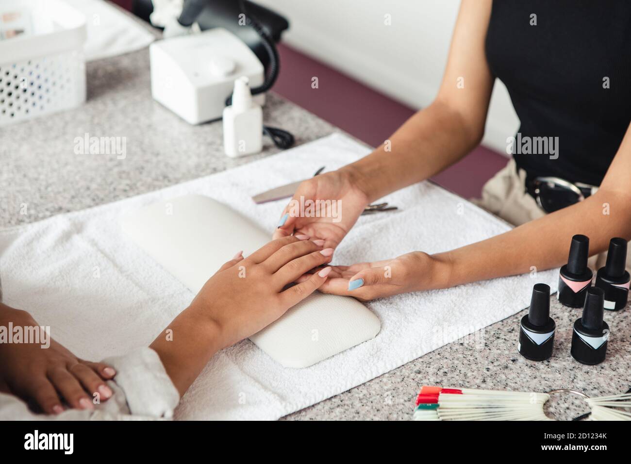 Reopening of beauty salon and a lot of work. Manicurist checks nails african american woman on table with equipment and bottles of varnish Stock Photo
