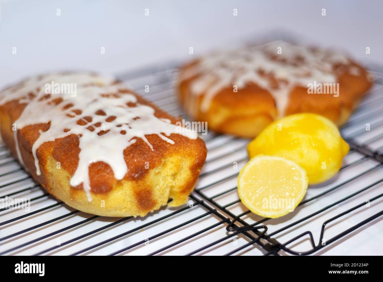 Two whole home made lemon drizzle cakes on a wire cake cooling rack