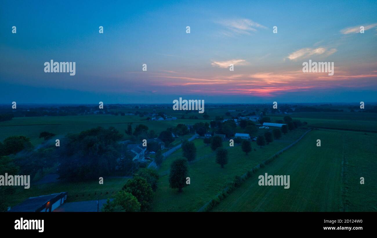 Aerial view of a summer sunset over farm lands with blue skies and red ...