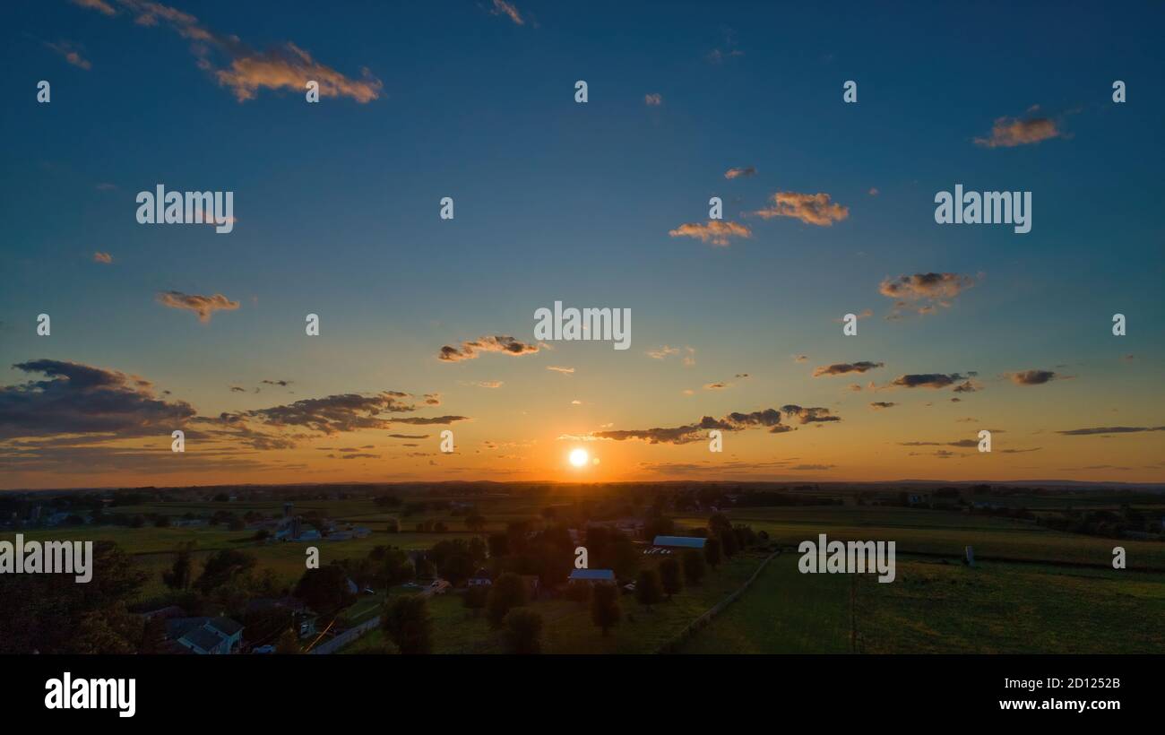 Sunset over barns, silos and green farmlands with blue, red and orange ...