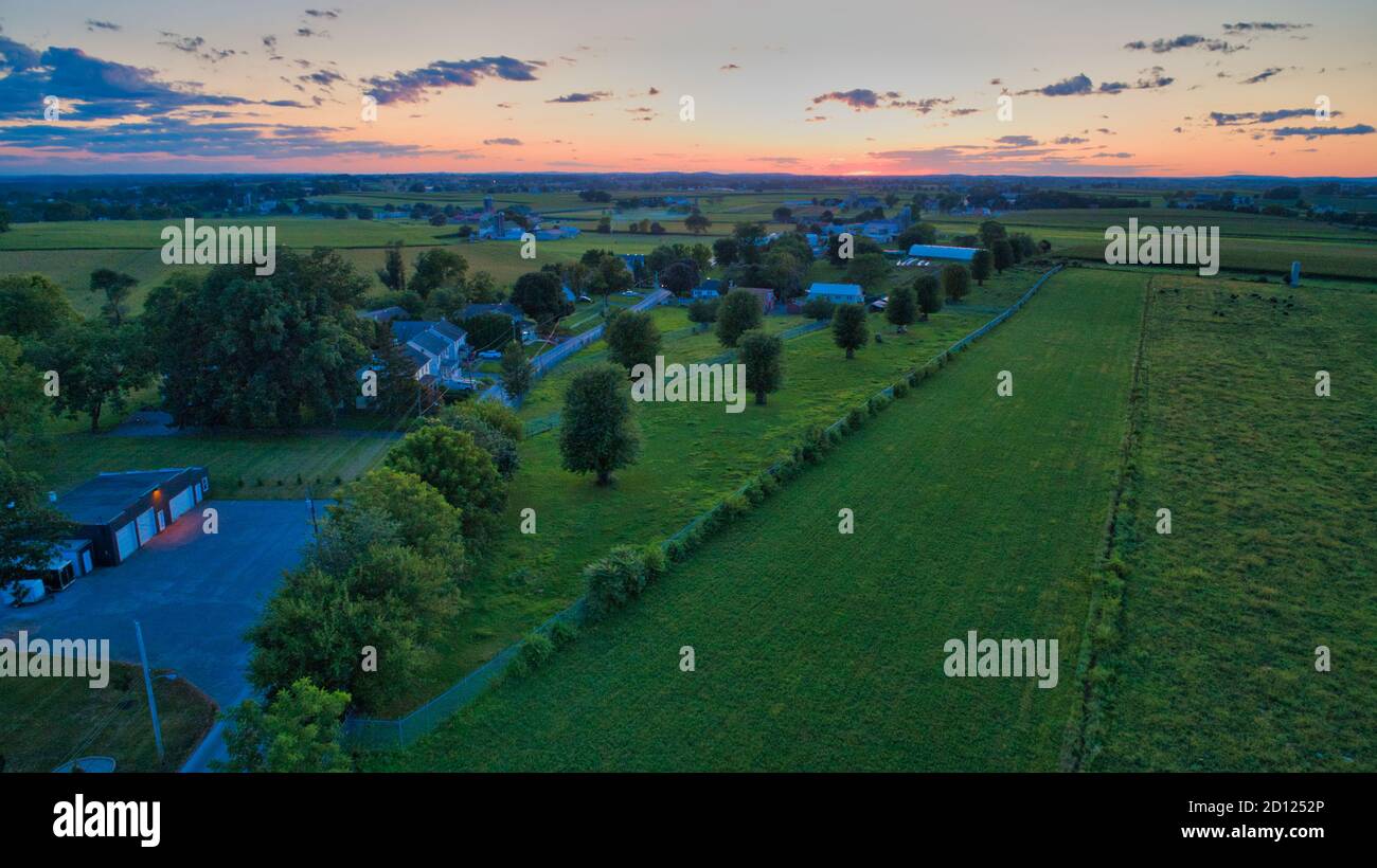 Sunset over barns, silos and green farmlands with blue, red and orange ...