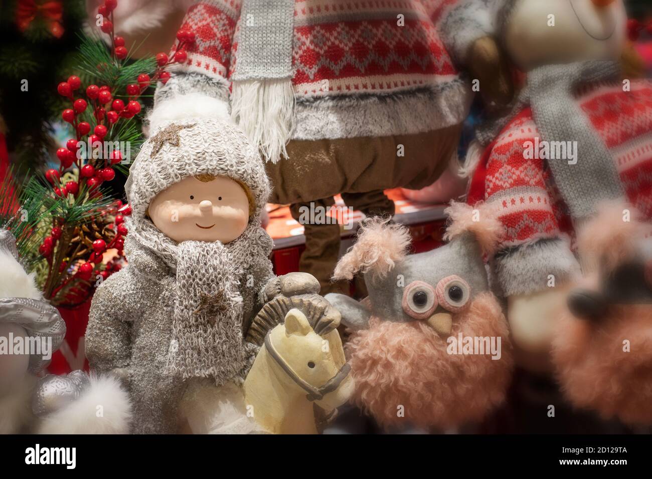 Cute baby doll in a winter costume on a horse, knitted hat and scarf. Rag fluffy owl and other Christmas toys gifts. Blurred background backdrop desig Stock Photo