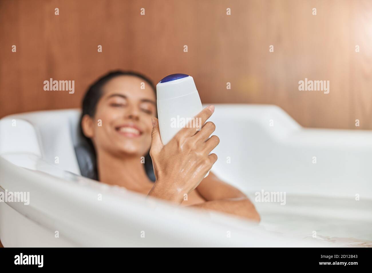 Charming young woman holding shower gel while taking bath Stock Photo