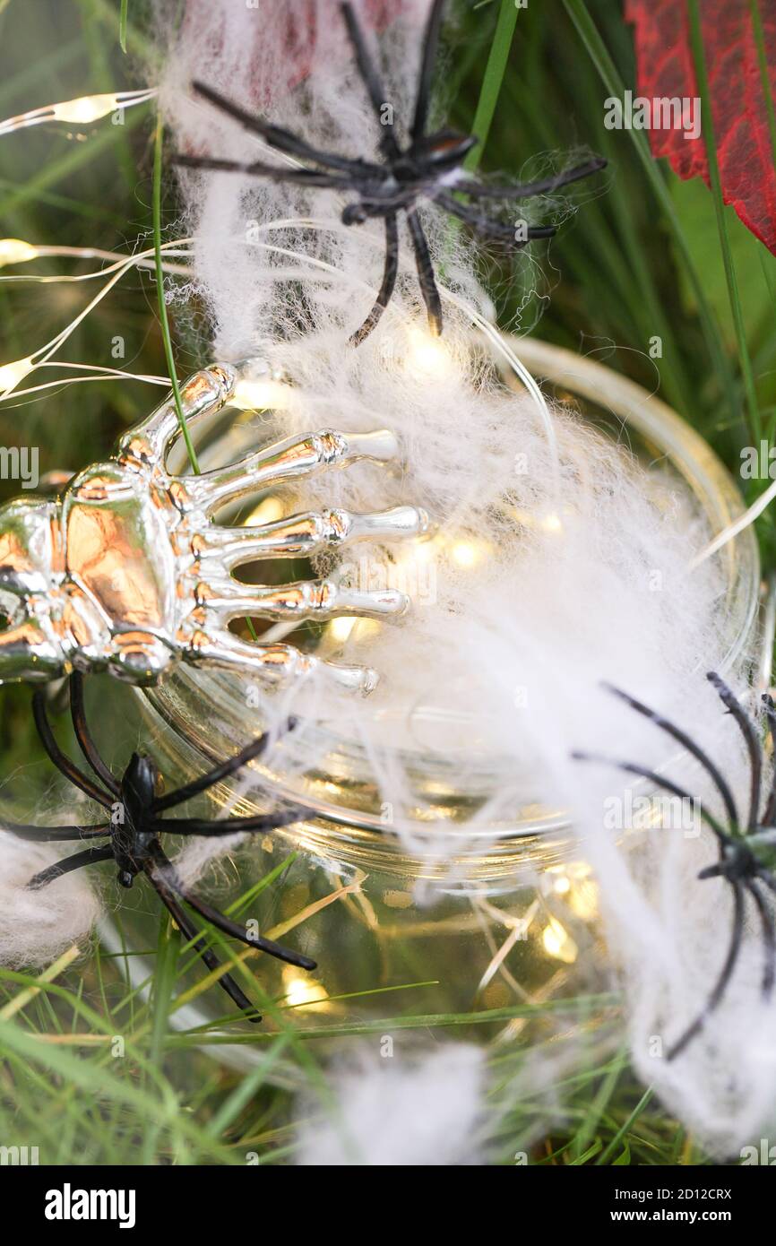 spider web and spiders in glass jar with garland and skeleton hand on green grass. halloween holiday concept  Stock Photo