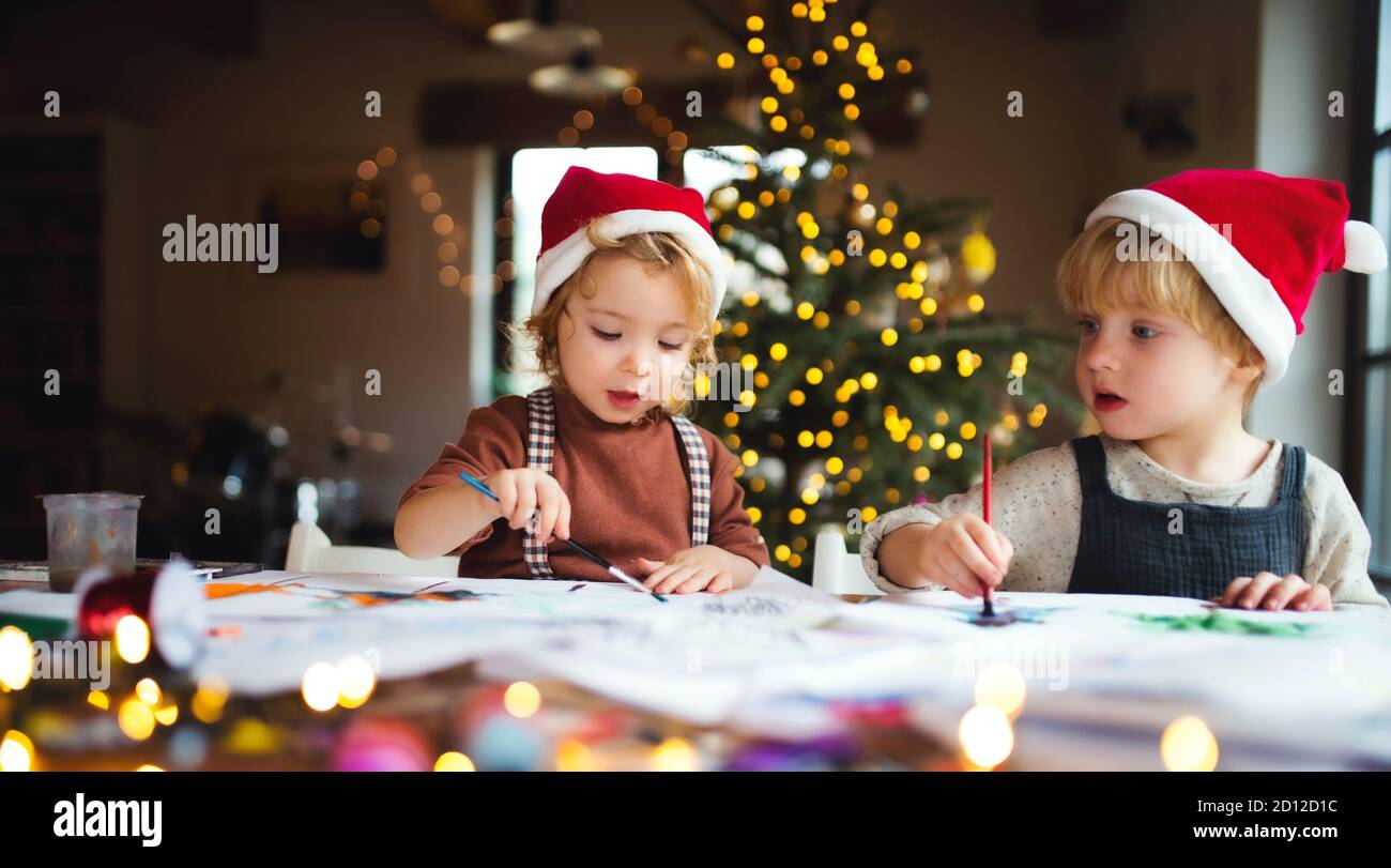 Portrait of small girl and boy indoors at home at Christmas, painting pictures. Stock Photo