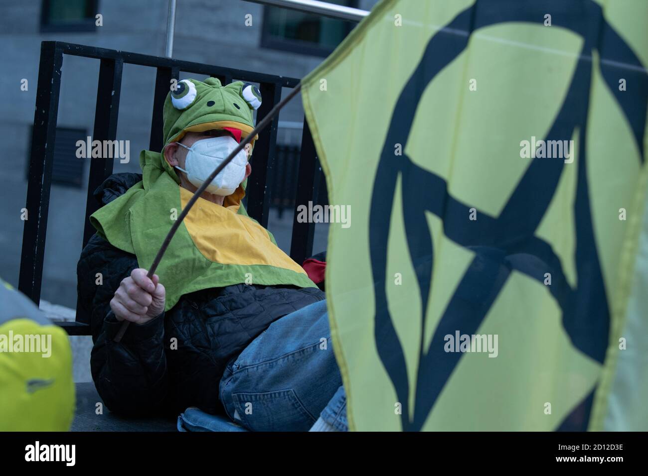 05 October 2020, Berlin: An environmental activist from Extinction Rebellion (XR) sits with a flag with the XR logo at an entrance to the Federal Ministry of Transport during a protest against the destruction of the environment by vehicles and the construction of new roads. This week, Extinction Rebellion has announced protest actions against environmental destruction and climate change. Photo: Paul Zinken/dpa Stock Photo