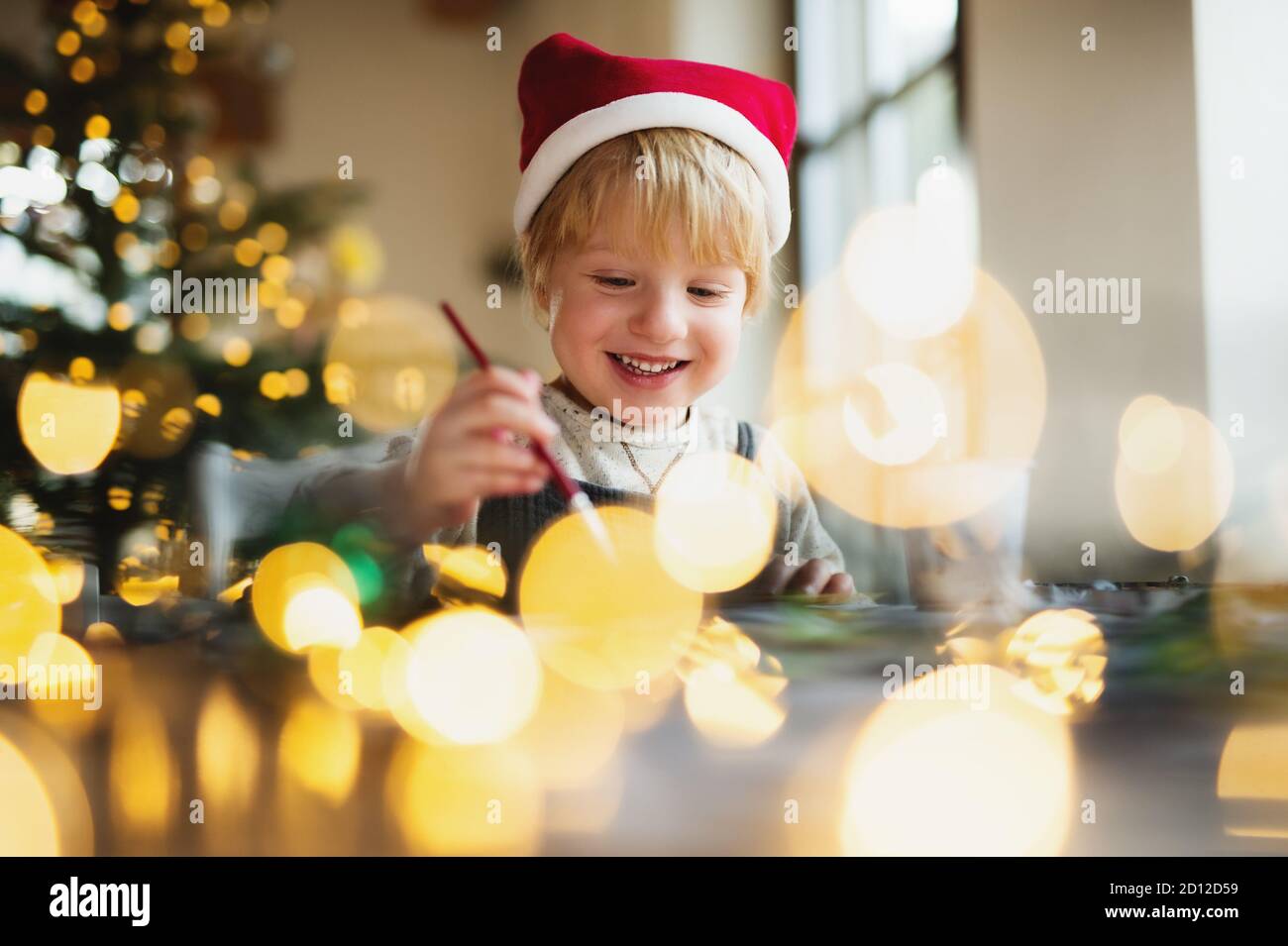 Portrait of small boy indoors at home at Christmas, painting pictures. Stock Photo