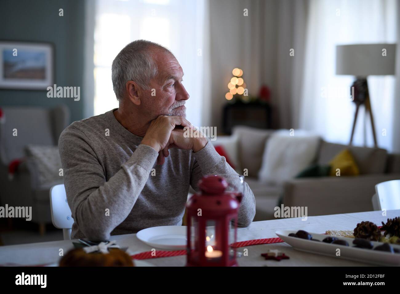 Lonely senior man sitting at the table indoors at Christmas, solitude concept. Stock Photo