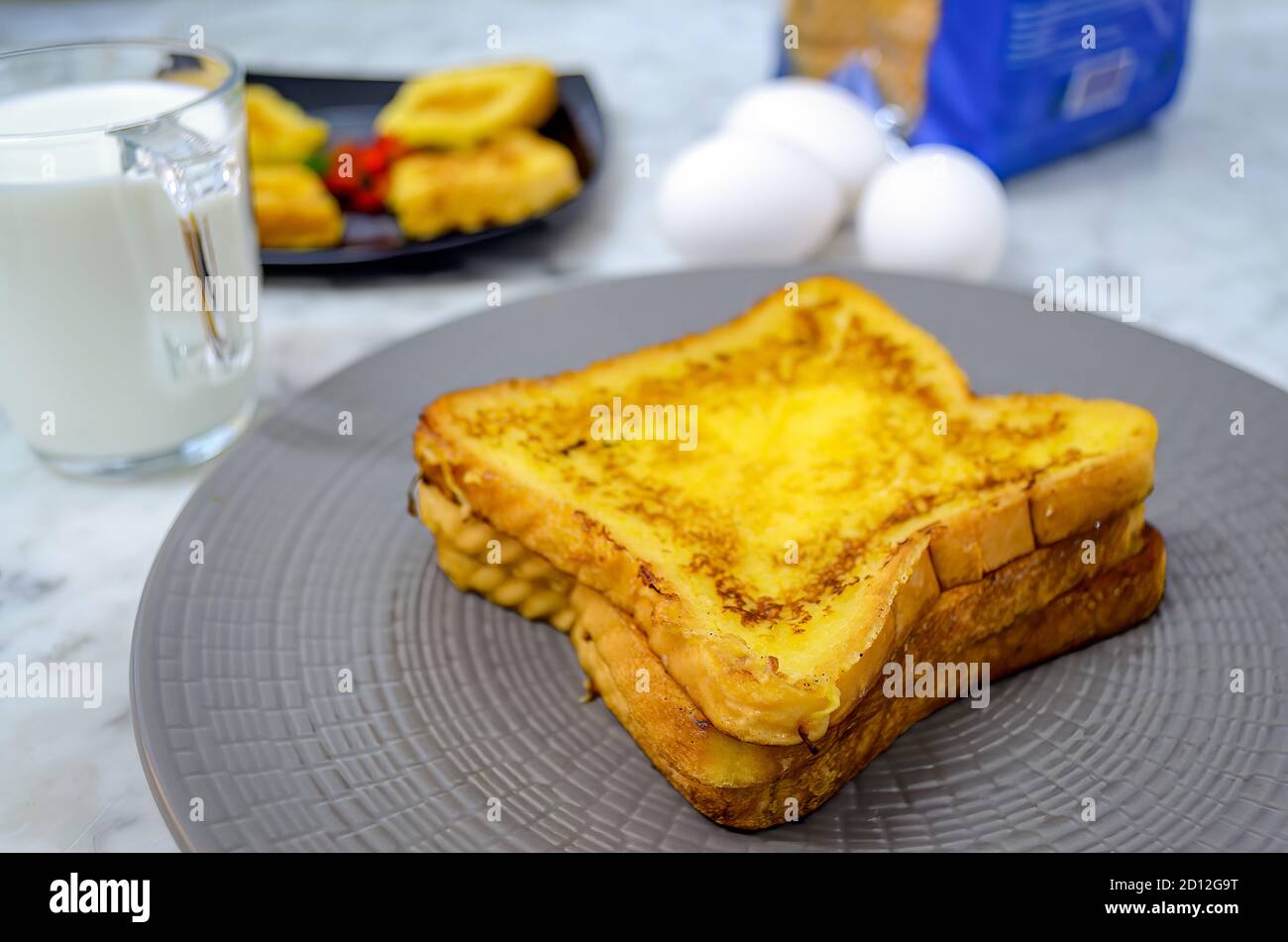 Beautifully Stacked French Toast in a plate along with milk, eggs, bread packet Stock Photo