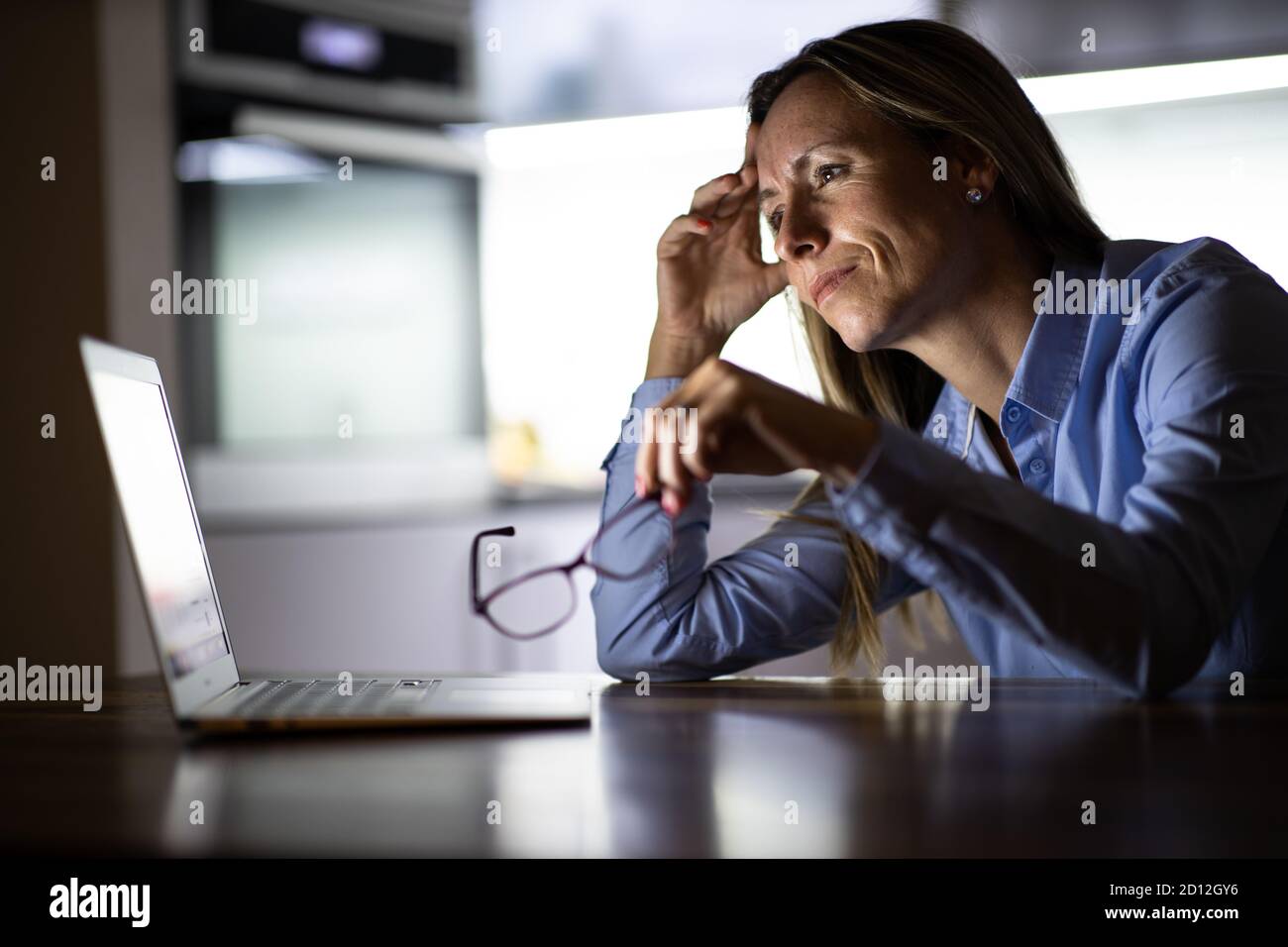 Pretty, middle-aged woman working late in the day on a laptop computer at home, running a business from home/working remotely for a corporation Stock Photo