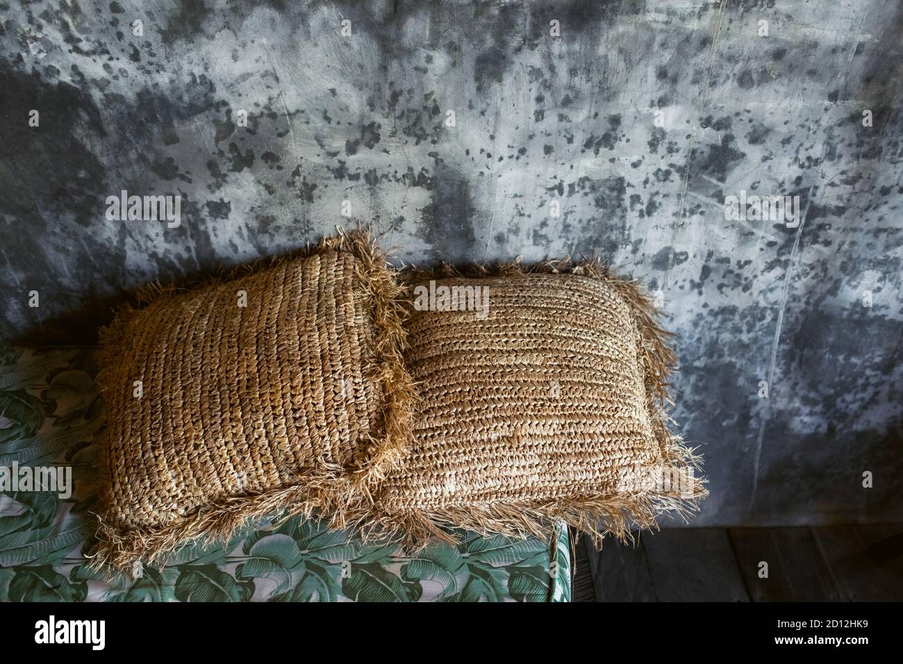 Two straw pillows as decoration in trendy loft interior. Gray concrete cement wall background