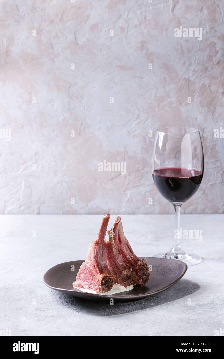 Grilled sliced rack of lamb with yogurt mint sauce served on ceramic plate with glass of red wine over grey texture table. Copy space Stock Photo