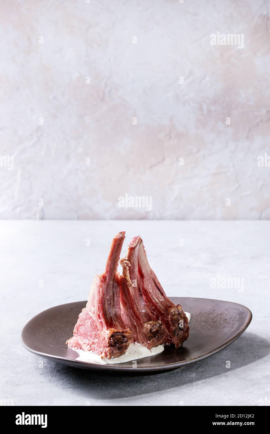 Grilled sliced rack of lamb with yogurt mint sauce served on ceramic plate over grey texture table. Copy space Stock Photo