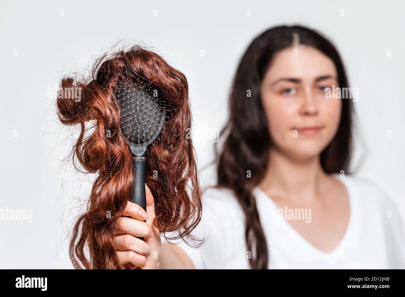 Blurred portrait of a woman holds a comb with a wig on it. White background. Concept of hair care and hair loss. Stock Photo