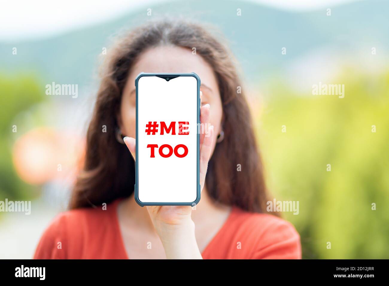 A woman holds a smartphone covering her face. Mock up. The concept of dependence on social networks and fake news. Stock Photo