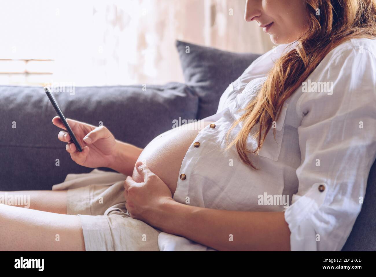 Pregnant woman using cell phone at her home. Stock Photo