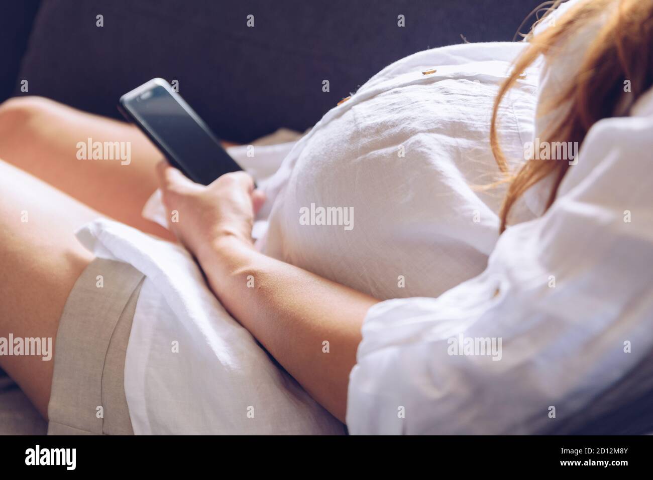 Pregnant woman using cell phone at her home. Stock Photo