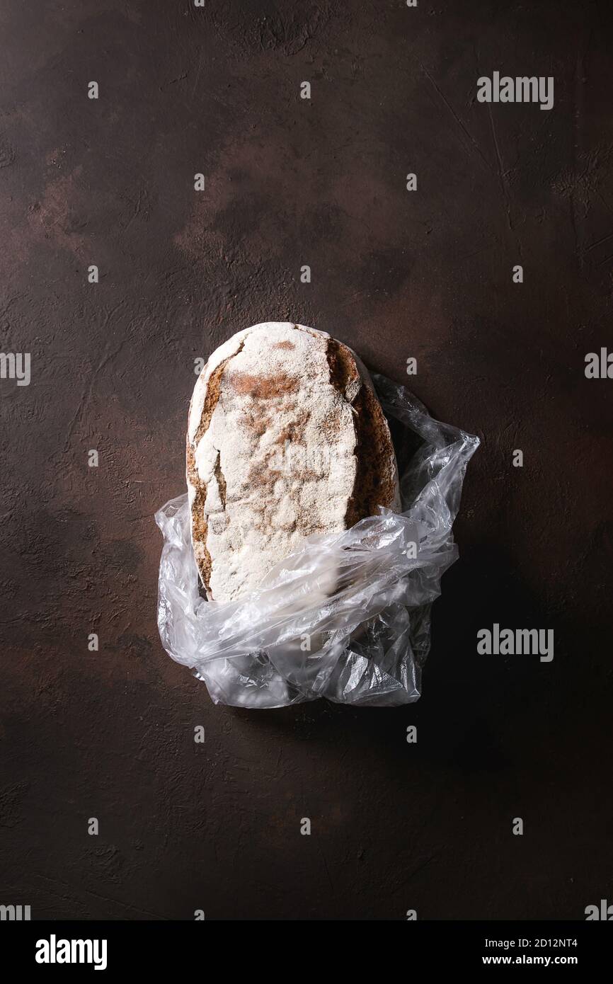 Loaf of fresh baked artisan rye bread in plastic bag over dark brown ...