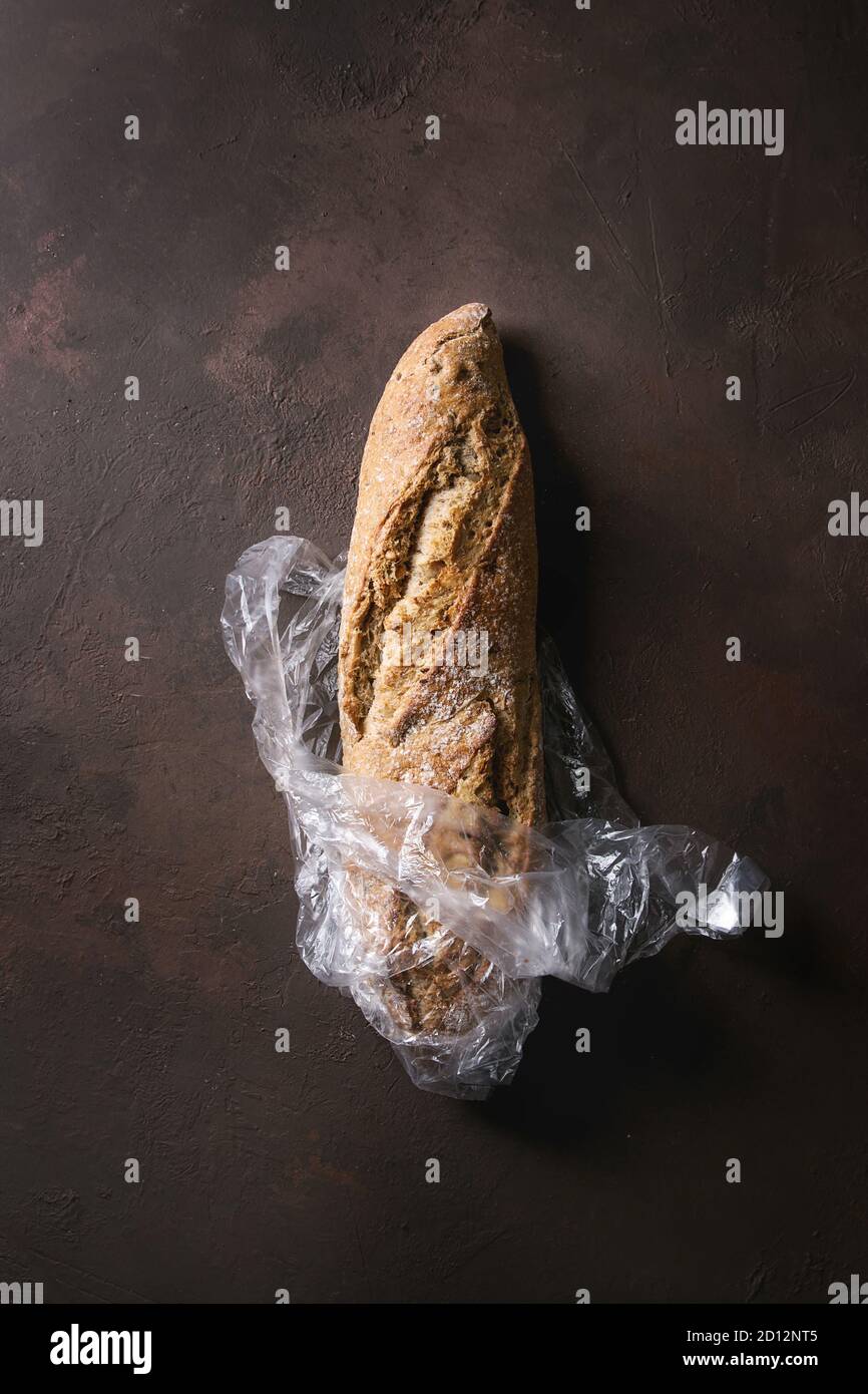 Loaf of fresh baked artisan whole grain bread in plastic bag over dark ...