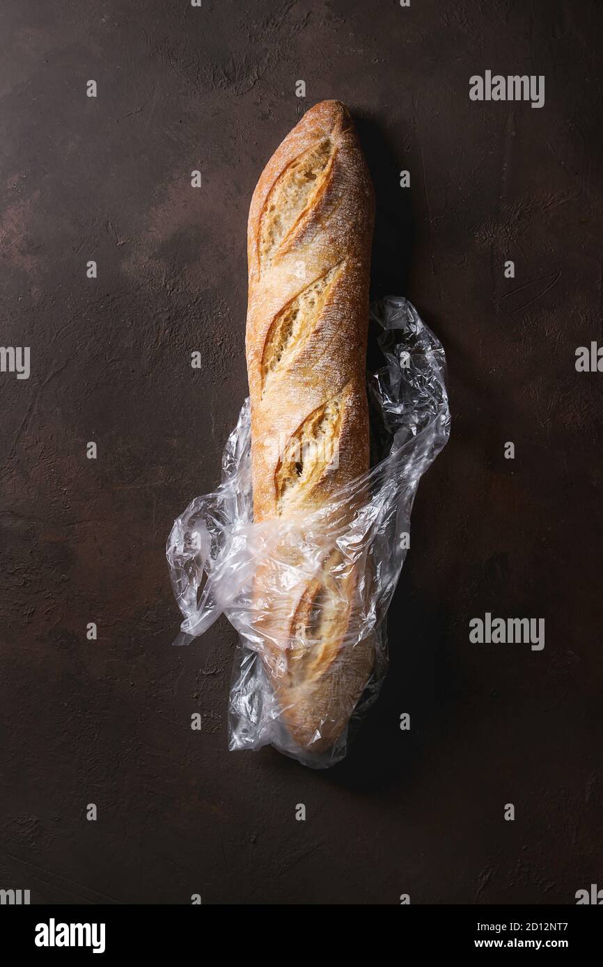 Loaf of fresh baked artisan baguette bread in plastic bag over dark ...