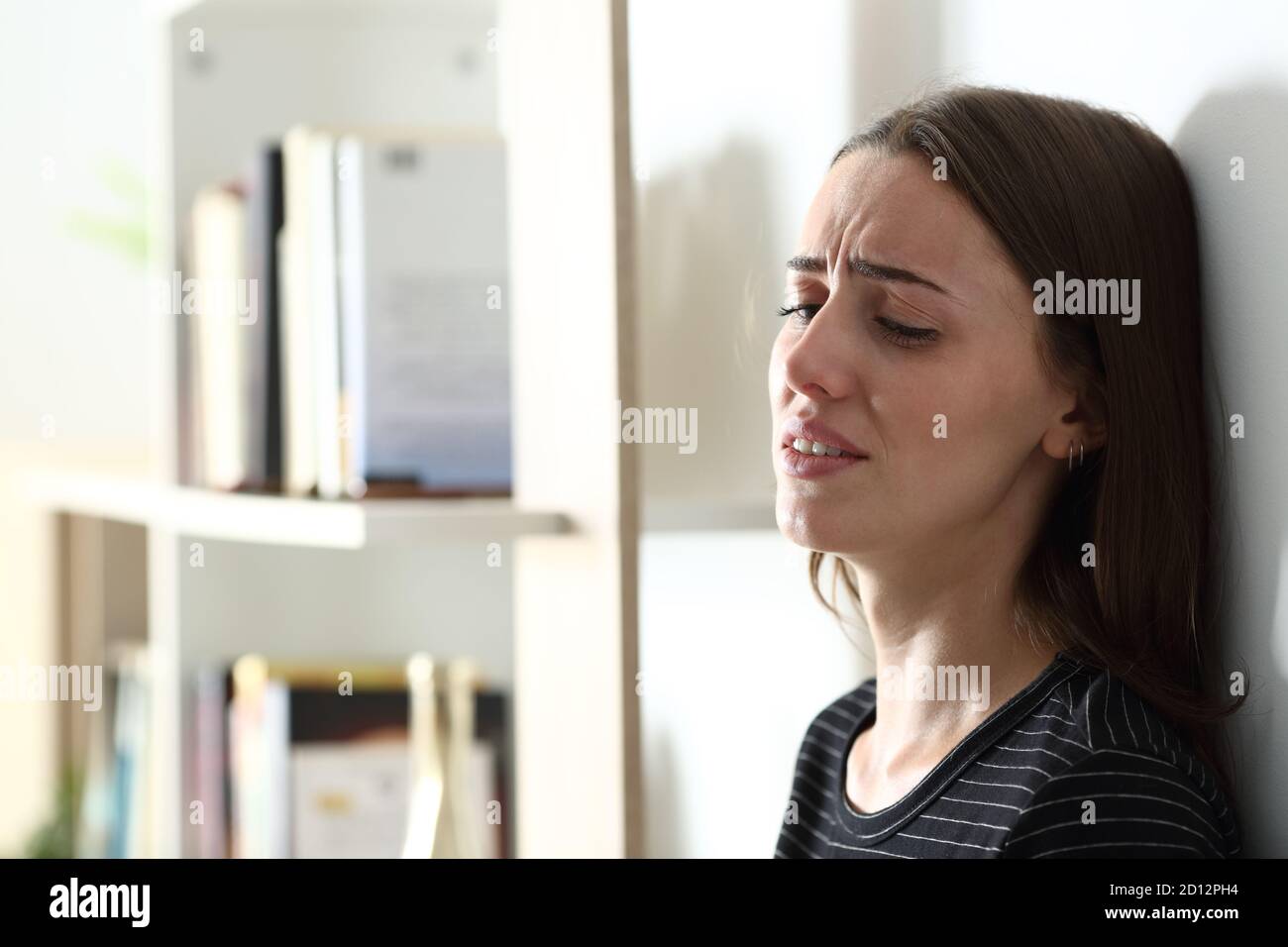 Depressed woman crying alone leaning on a wall at home Stock Photo