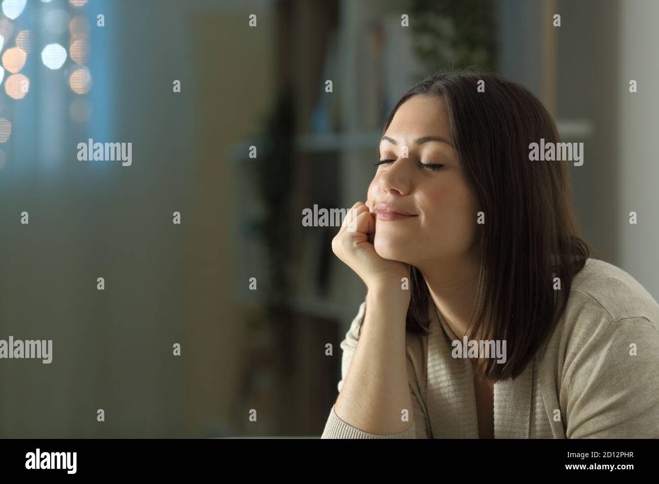 Woman relaxing mind in the living room at home in the night with a window in the background Stock Photo