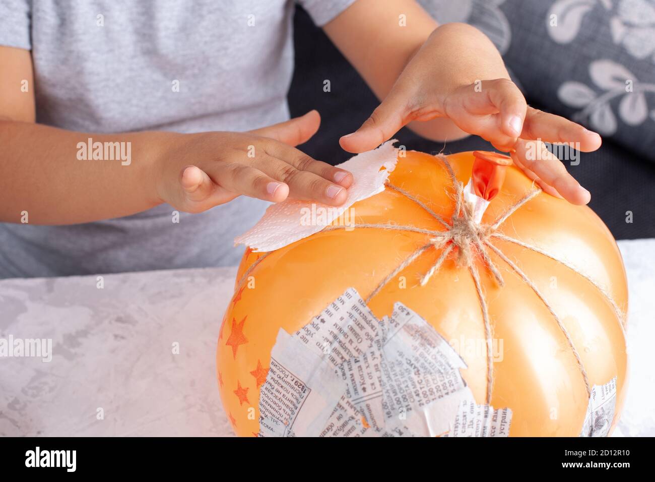 a child's hands glue napkins to a balloon to make a papiermache