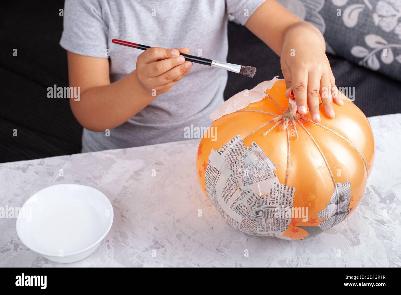 a child puts glue on a balloon to stick pieces of paper, makes a pumpkin out of papiermache