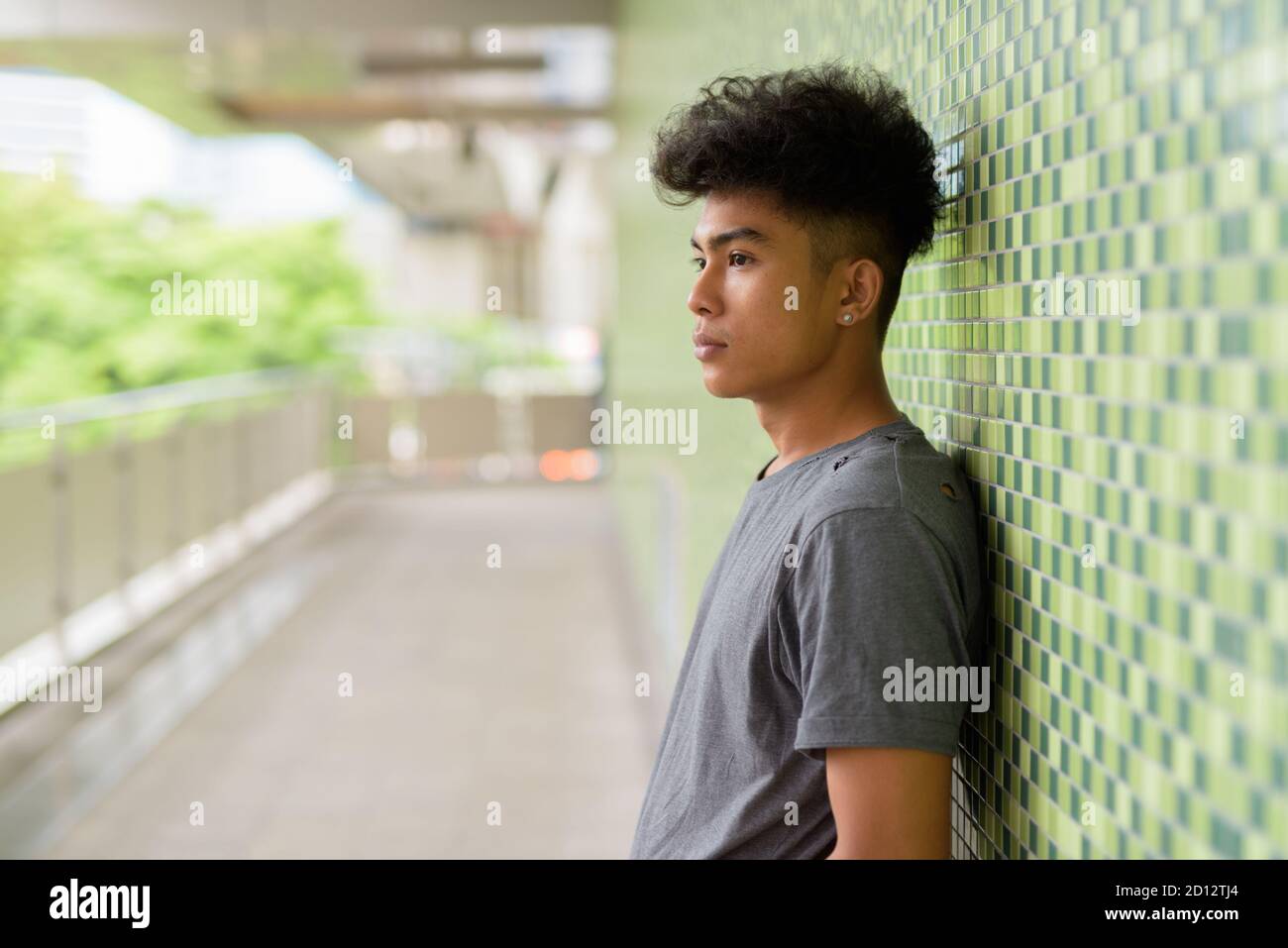Profile view of young Asian man with curly hair at footbridge in the city Stock Photo