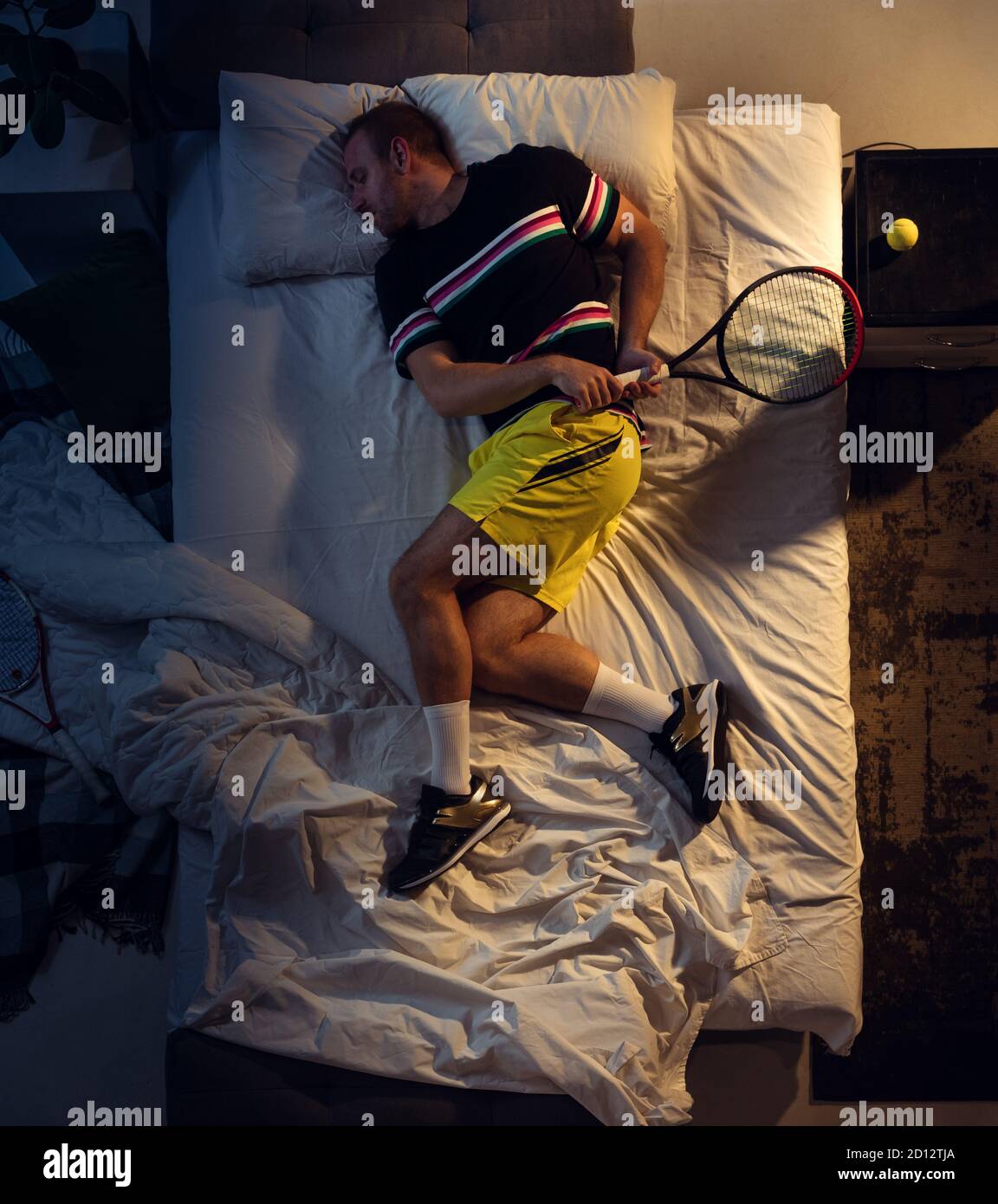 In love. Top view of young professional tennis player sleeping at his  bedroom in sportwear with racket. Loving his sport even more than comfort,  watching match even if resting. Action, motion, humor
