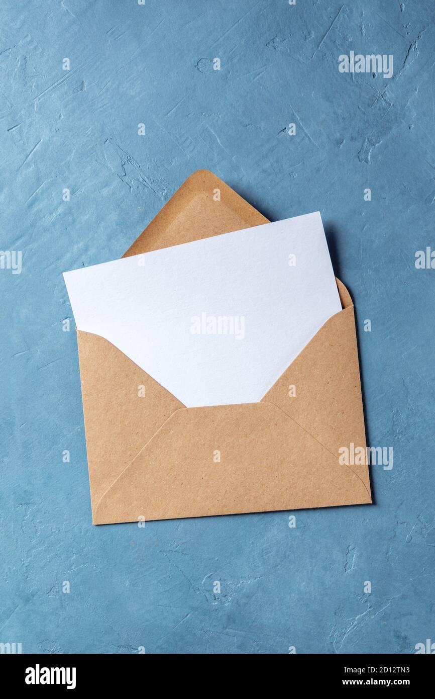 Autumn stationery mockup, top flat lay shot of an A5 greeting card or invitation in a brown kraft envelope, on a blue background Stock Photo