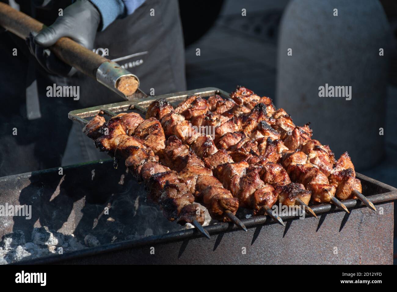 Close up of meat skewer, grilled in a barbecue, shashlik or shashlyk of pork for a picnic, man preparing and roasting with pitchforks Stock Photo