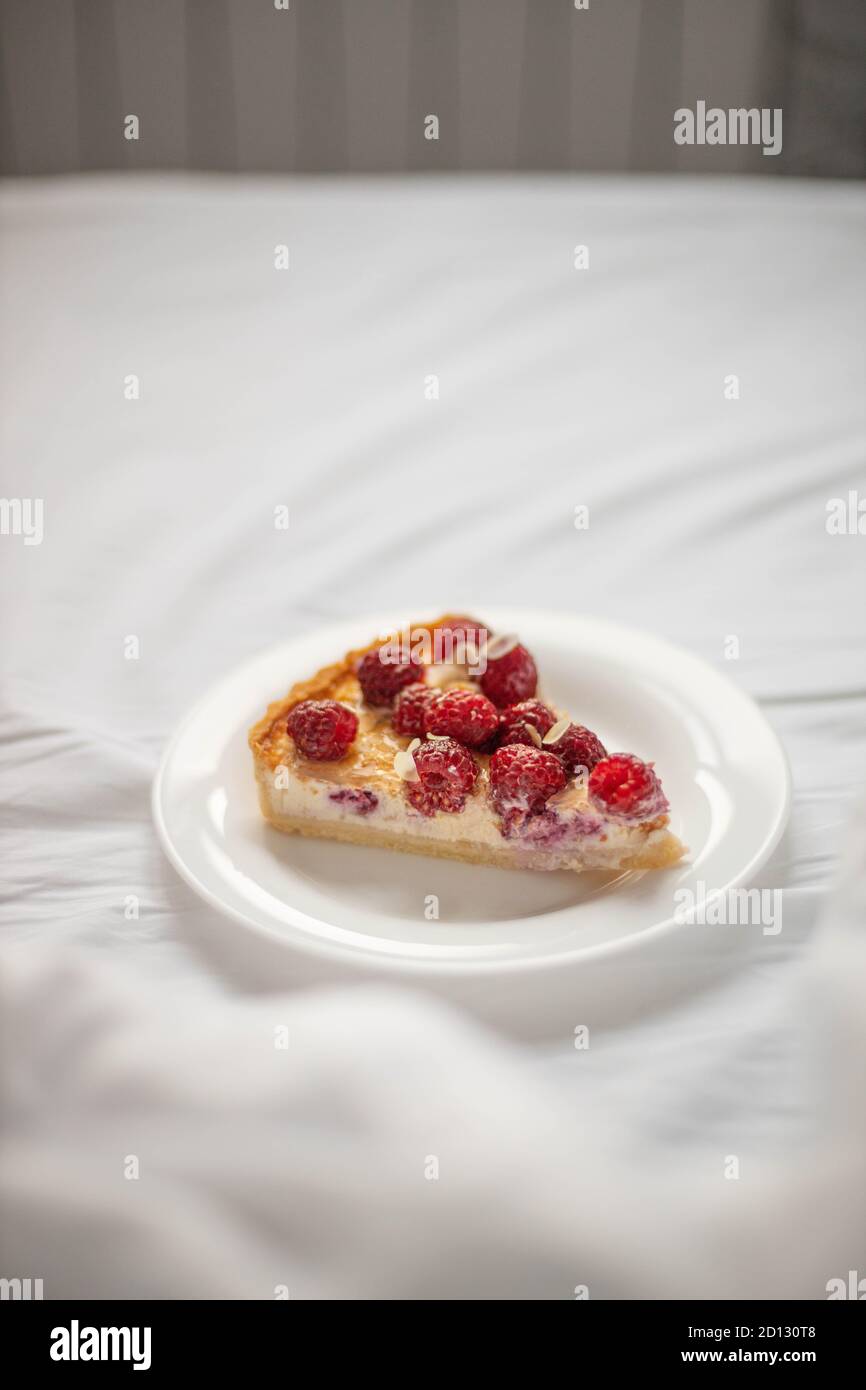 Piece of classic cheesecake with raspberry berries on a white plate on the bed. Vertical orientation Stock Photo
